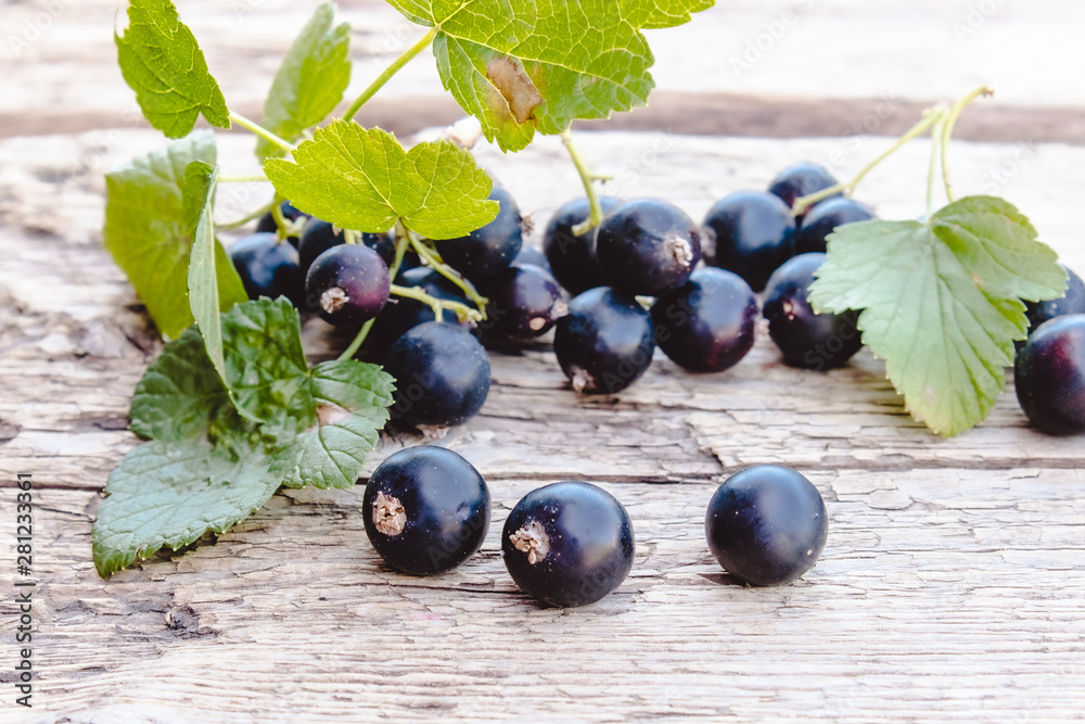 Black currant lies next to the green leaves on a wooden background. Juicy natural fruits currant. Black currant lies next to the green leaves on a wooden background. Juicy natural fruits currant.