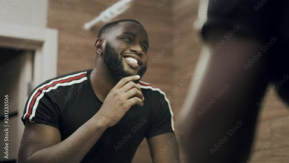 Black man standing in front of mirror at bathroom. Portrait of smiling man.