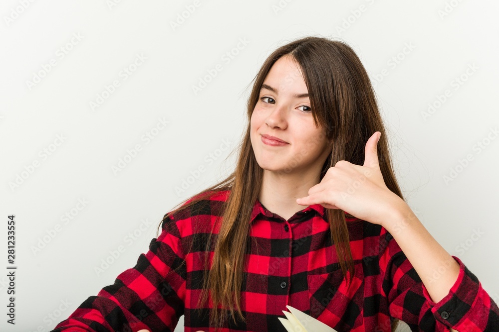 Young teenager going back to her routine doing homeworks showing a mobile phone call gesture with fingers. Young teenager going back to her routine doing homeworks showing a mobile phone call gesture with fingers.