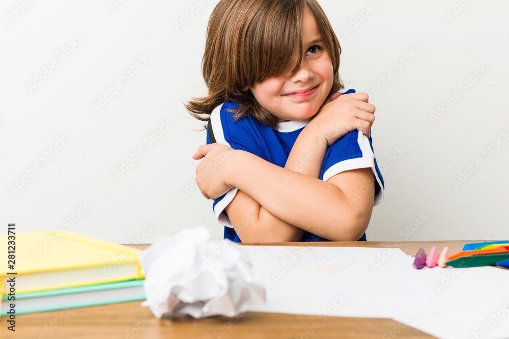 Little boy painting and doing homeworks on his desk hugs, smiling carefree and happy.
