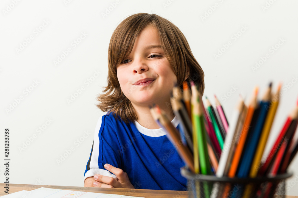 Little boy painting and doing homeworks on his desk frowning face in displeasure, keeps arms folded. Little boy painting and doing homeworks on his desk frowning face in displeasure, keeps arms folded.