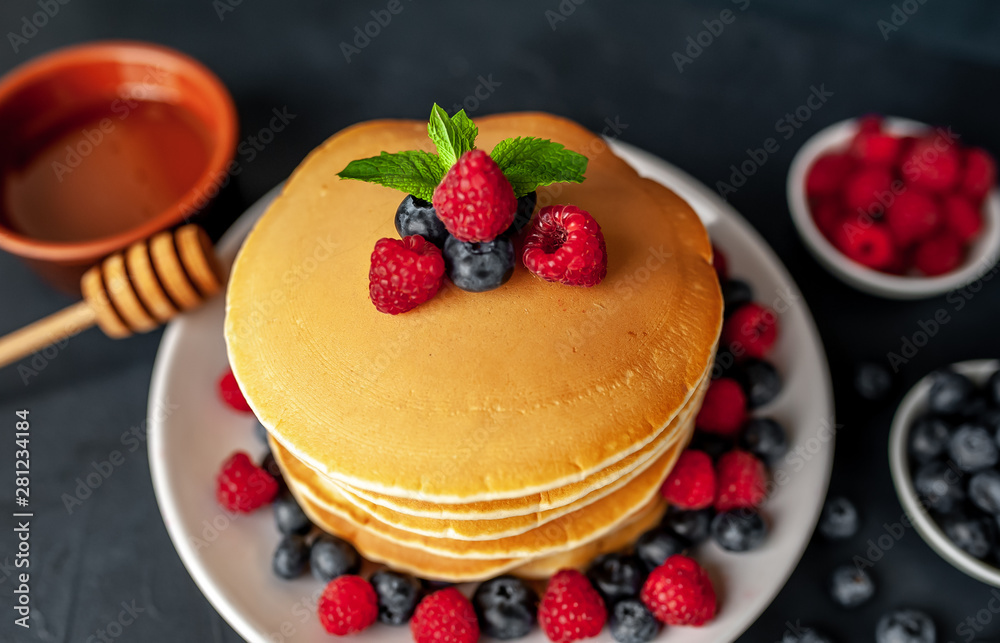 American pancakes with raspberries, fresh blueberries and honey. Healthy morning breakfast on concrete background