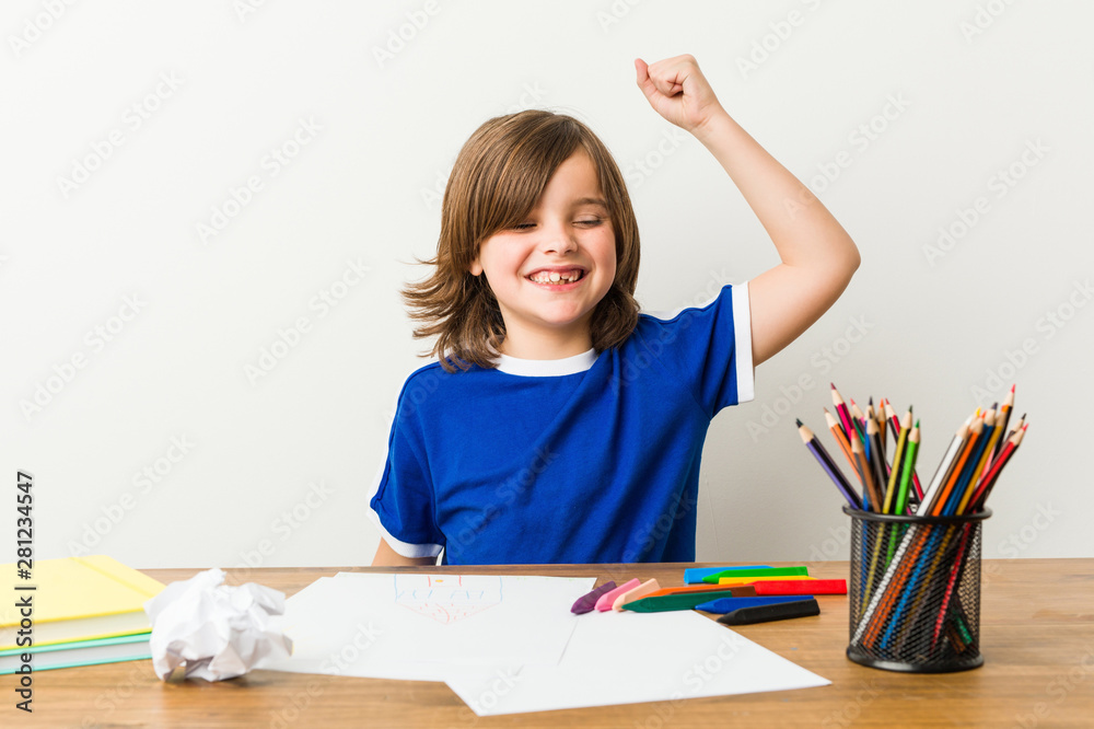 Little boy painting and doing homeworks on his desk raising fist after a victory, winner concept. Little boy painting and doing homeworks on his desk raising fist after a victory, winner concept.