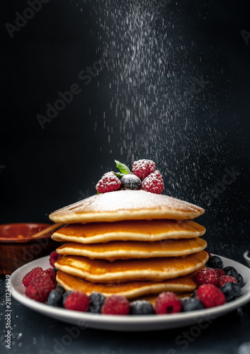 American pancakes with raspberries, fresh blueberries and honey. Healthy breakfast on concrete background, sprinkled with powdered sugar on pancakes