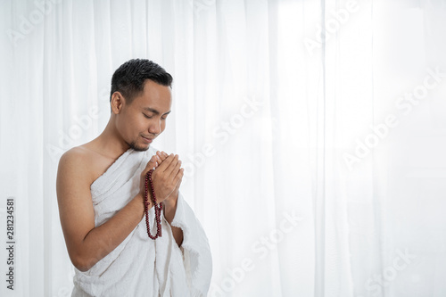 muslim young man praying using tasbih while standing in white traditional clothes photo