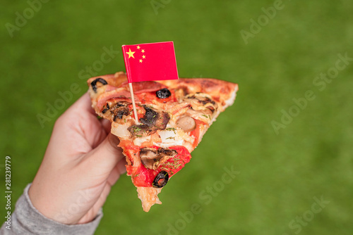 A slice of pizza in female hands with Chinese flag in the form of a toothpick. Lunch on the green grass. China. Concept