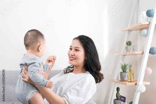 Young mother with her one years old little son dressed in pajamas are relaxing and playing in the living room at the weekend together, lazy morning, warm and cozy scene. Selective focus.