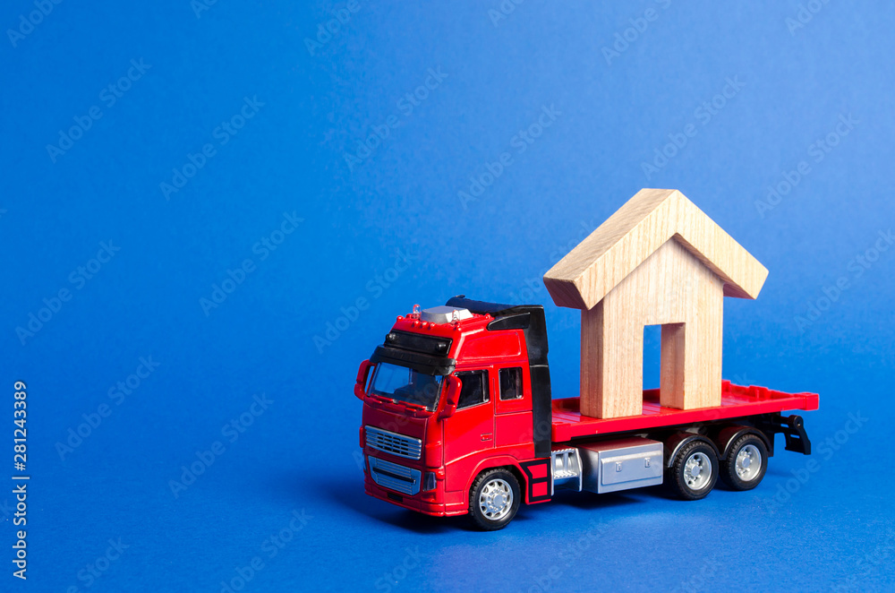 A red truck transports a wooden house. Concept of transportation and cargo shipping, moving company. Construction of new houses and objects. Industry. Logistics and supply. Move entire buildings.