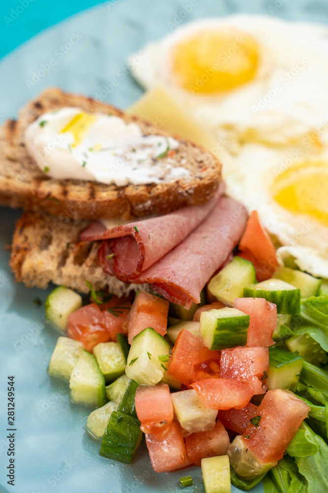 Close up of hotel breakfast with fried eggs, toasts with ham and cheese and summer salad