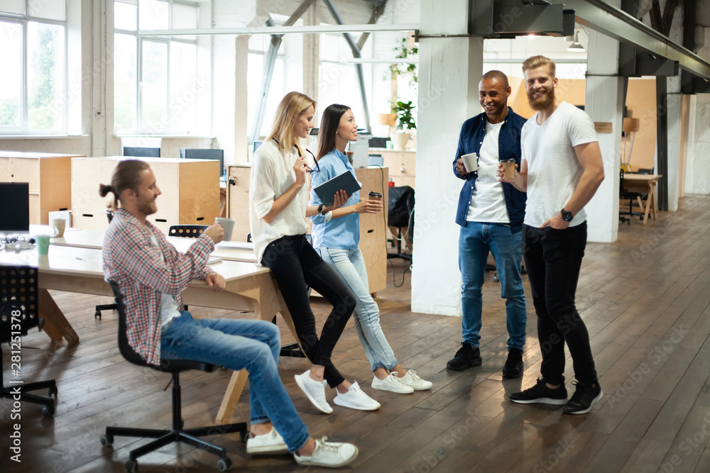 Young modern colleagues in smart casual wear working together while spending time in the creative office.