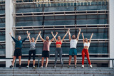 Full length of young people in sports clothing keeping arms outstretched and smiling while standing outdoors