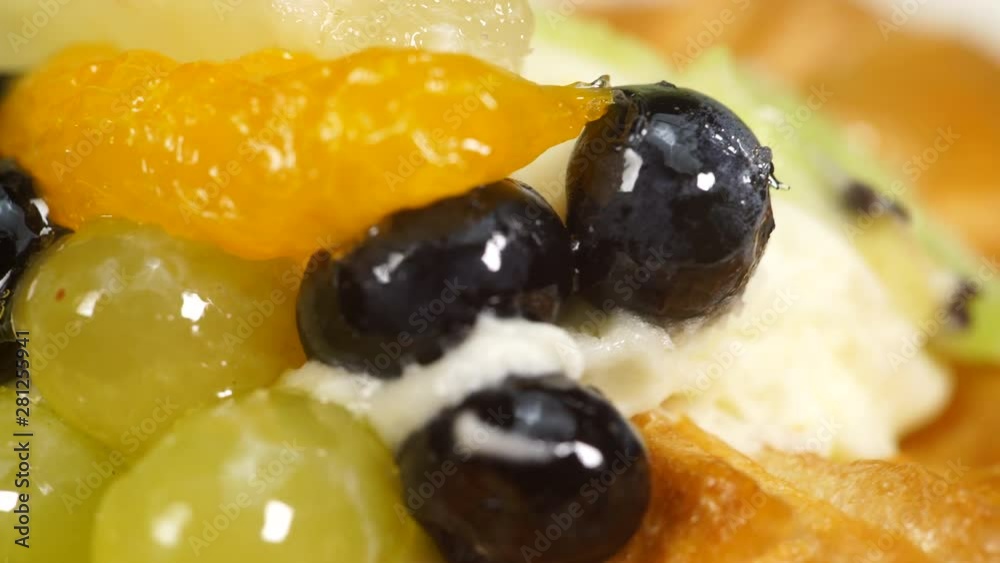 Close up puff pastry pie decorated with fresh blueberry and fruit slices - kiwi, grapes, ananas. Cake rotating