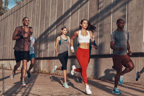 Fototapeta Naklejka Na Ścianę i Meble -  Full length of people in sports clothing jogging while exercising on the sidewalk outdoors