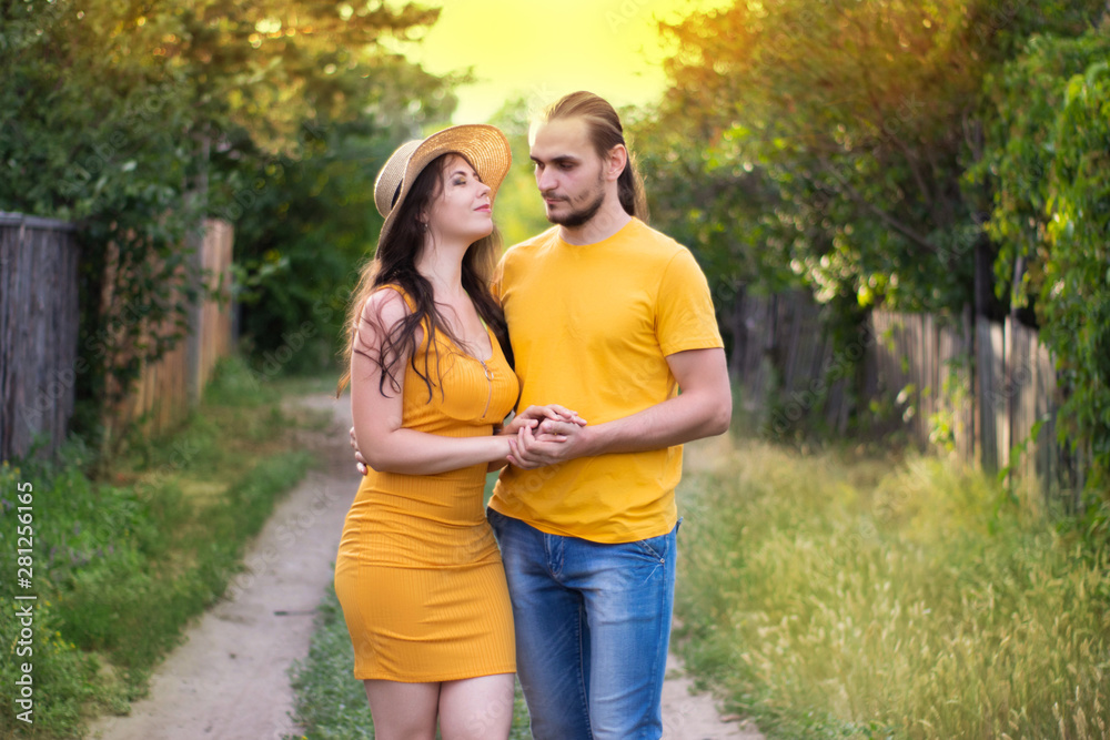 Fototapeta premium Young woman in a hat and a man walking down the street. Portrait of a couple in love. Summer mood, hot sunny day.