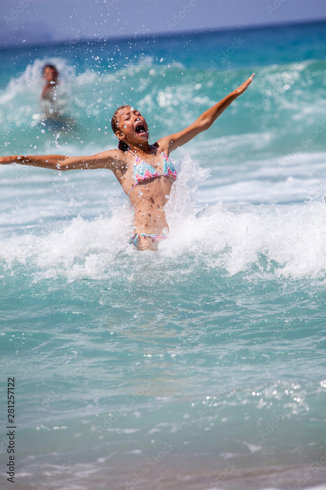 Young girl laughing and crying in the spray of waves at sea on a sunny day. Young girl laughing and crying in the spray of waves at sea on a sunny day.
