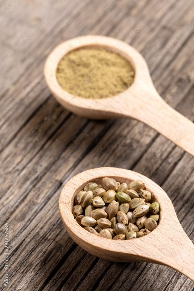 Two wooden spoons with cannabis grains and flour on  diagonal old wooden boards. 