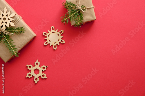 New year or Christmas composition. Presents wrapped kraft paper and fir tree branches, wooden handmade snowflakes decorations on red background. Flat lay, top view, copy space, Christmas banner mockup