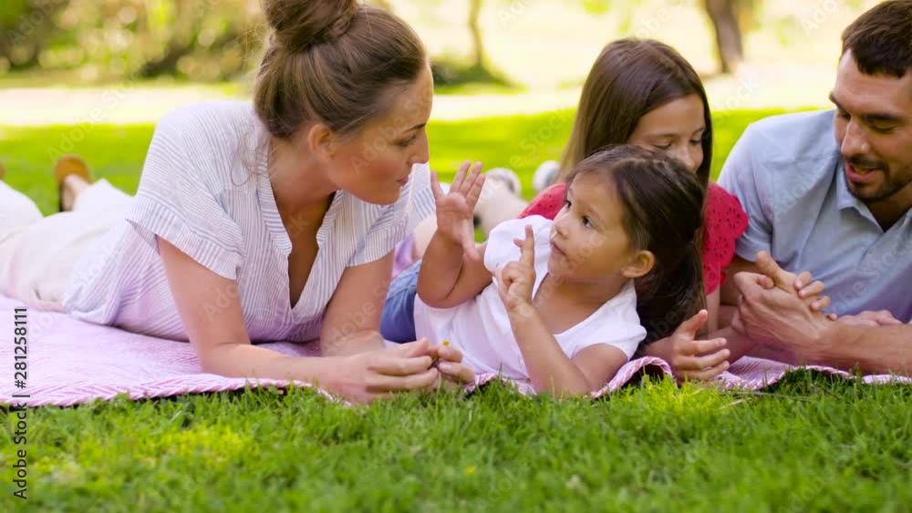 family, leisure and people concept - happy mother, father and two daughters lying on picnic blanket and talking in summer park family, leisure and people concept - happy mother, father and two daughters lying on picnic blanket and talking in summer park