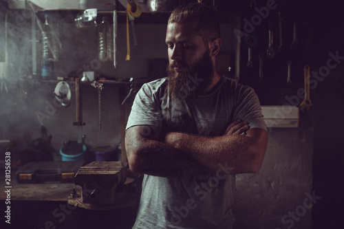 Handsome brutal man with a beard standing in his garage against the background of repair tools