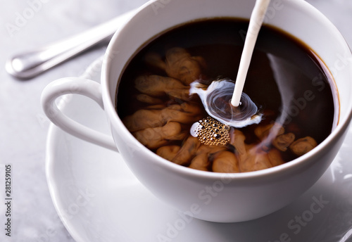 Caffè latte in white cup with pouring milk and light background