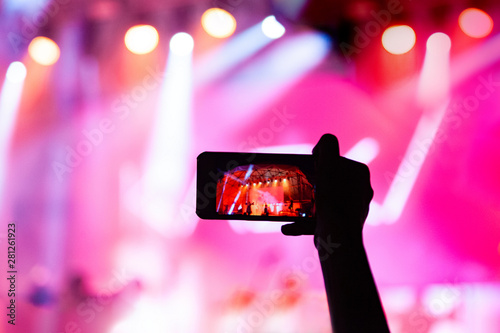 Raised hand of a man with a smartphone in front of bright lights record a concert.