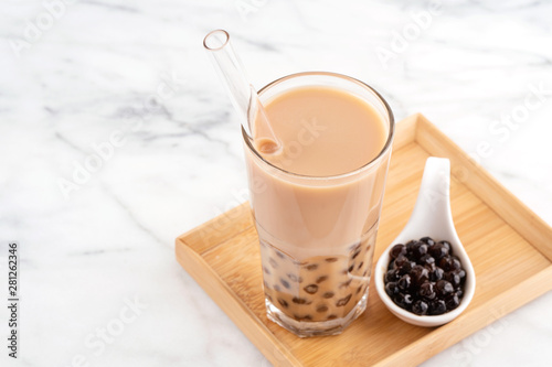 Tapioca pearl ball bubble milk tea, popular Taiwan drink, in drinking glass with straw on marble white table and wooden tray, close up, copy space.