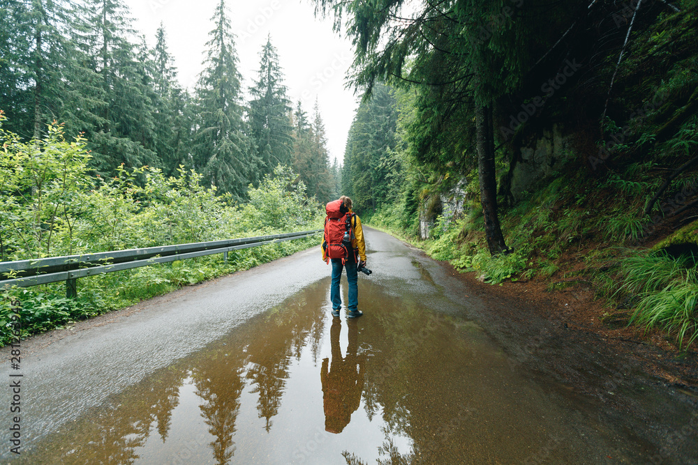 Man with hiking equipment walking in mountain forest. Active healthy man with backpack and camera hiking in beautiful forest