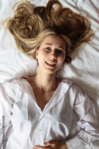 Portrait beautiful blonde woman with a beautiful face and amazing eyes, lies, sleeps on the bed linen in an elegant. And sensual looks and flirtatious smile. Health and harmony concept