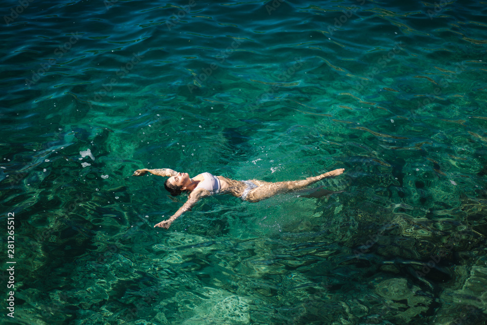 Sexy woman in bikini lying on the water. Attractive young woman enjoying summer sun. Beautiful lagoon. Woman swin in the sea. Top view