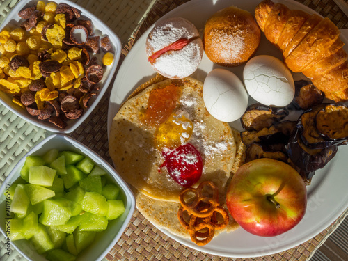 breakfast served with croissant, eggs, melon, flakes with milk, apple fruit, pancakes, mix of jams, eggplant slices. Balanced diet