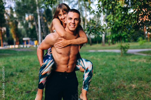 Couple man and woman have a fun time in the park outdoor. Girl hugging a guy behind