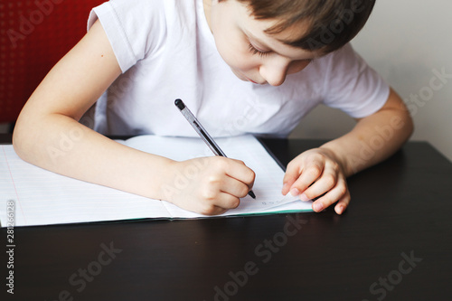 the child is studying. the boy sits at the table and writes in a notebook. child sits and does homework on a white background