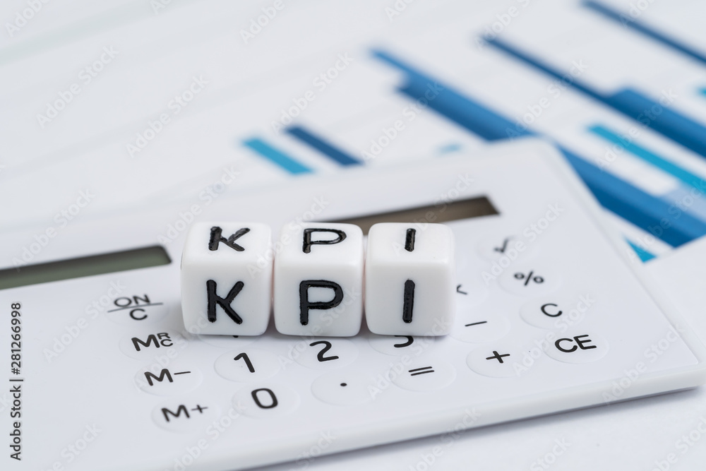 Key Performance Indicator, KPI measurement to evaluate business success, white cube block with alphabets building the word KPI on calculator over bar graph reports Key Performance Indicator, KPI measurement to evaluate business success, white cube block with alphabets building the word KPI on calculator over bar graph reports