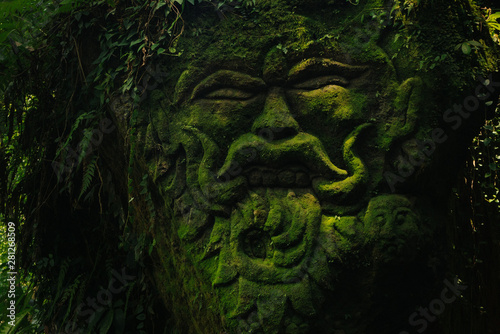 Vászonkép Carving demons faces on wall background covered with moss texture in Bali