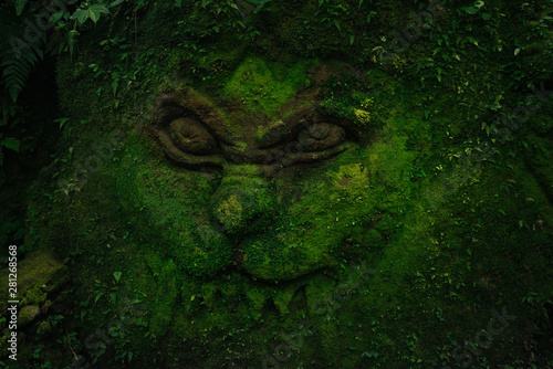 Carving demons faces on wall background covered with moss texture in Bali