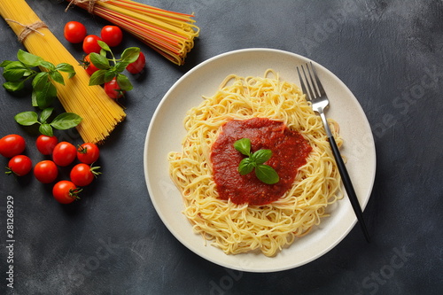 Classic Italian spaghetti pasta with tomato sauce and basil on plate on dark table
