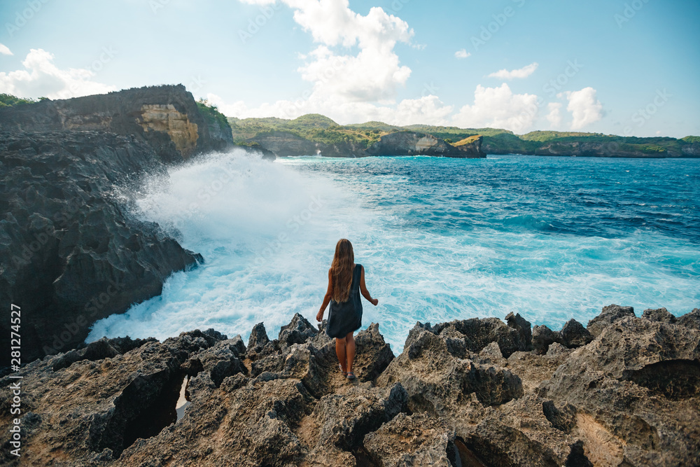 Girl traveler on the edge of the rock enjoys a beautiful view of the raging ocean,Bali,Nusa Penida island. The most beautiful places of the island of Bali and Nusa Penida