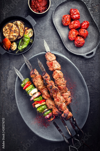 Traditional Russian shashlik on a barbecue skewer with vegetable and sumach paste as top view on a modern design plate