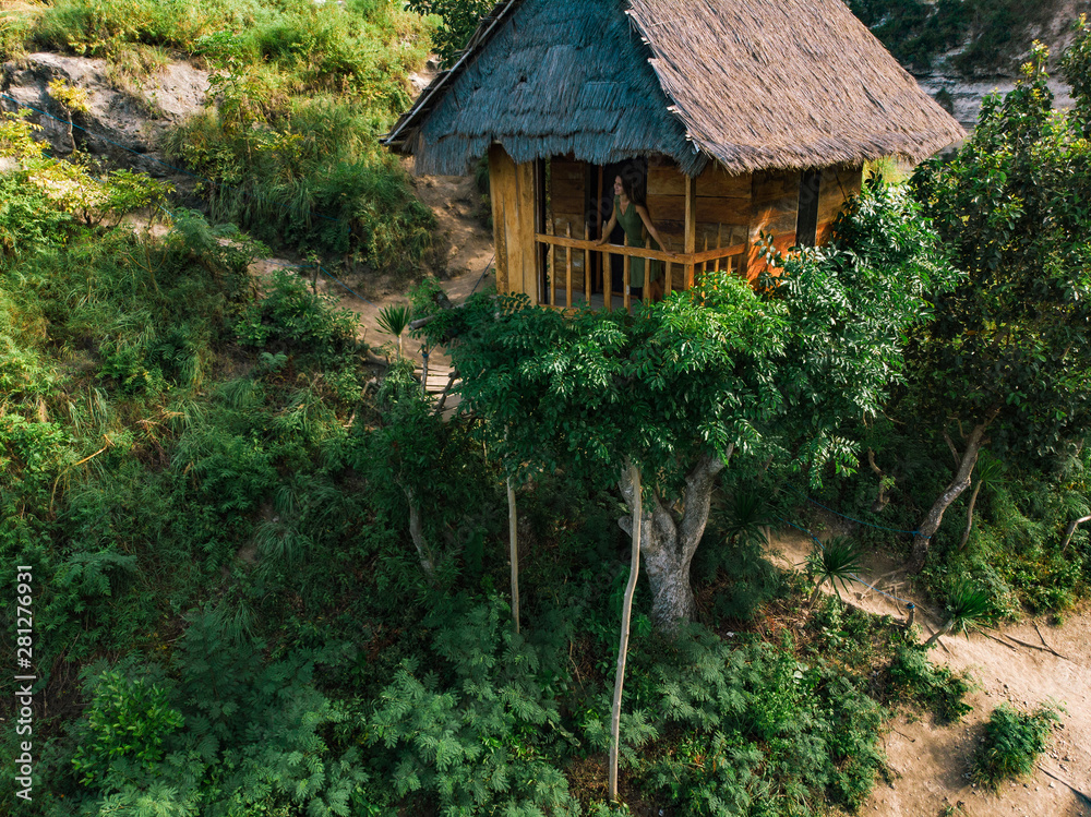 Young girl in Beautiful creative handmade tree house. Traditional house on tree, couple look at Atun beach, Nusa Penida island. Popular travel destination on Bali holidays. Indonesia Young girl in Beautiful creative handmade tree house. Traditional house on tree, couple look at Atun beach, Nusa Penida island. Popular travel destination on Bali holidays. Indonesia