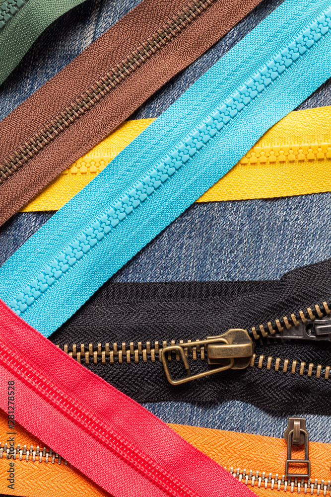 Pack a lot of colorful plastic and metal zippers stripes with sliders pattern for handmade sewing tailoring on the blue denim background close up selective focus