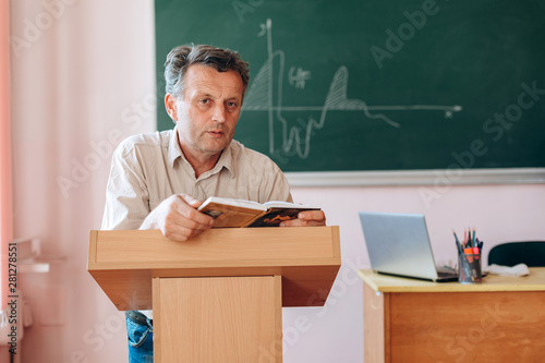 Middle age teacher holding a book and explain a lesson. Concept education.-Image