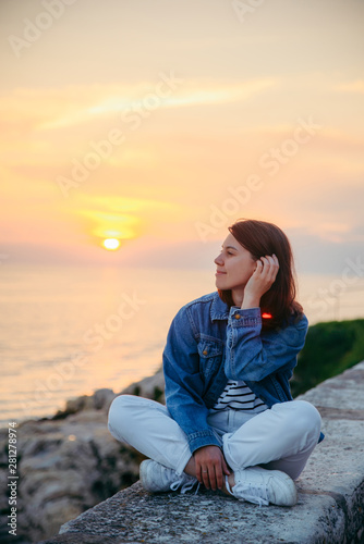 young pretty woman sitting at cliff looking on beautiful sunset