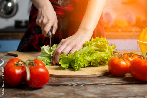 girl cut lettuce on a wooden table, a woman prepares a veggie salad, healthy food, a knife chops greens