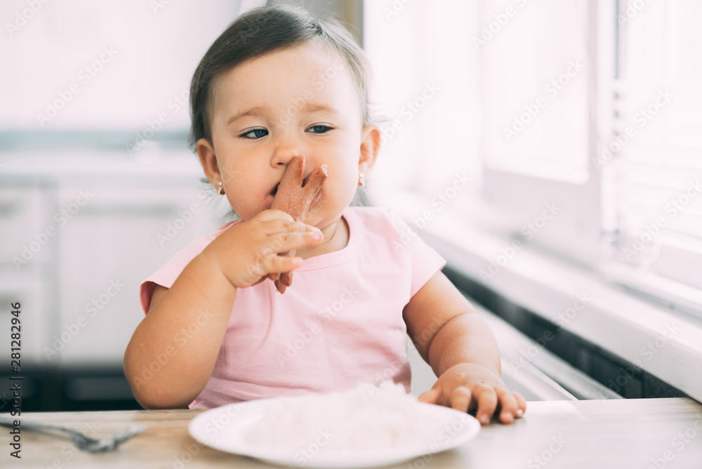 Little baby girl in the kitchen eating sausage and mashed potatoes Little baby girl in the kitchen eating sausage and mashed potatoes
