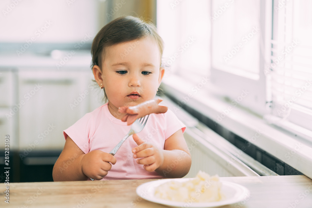 Little baby girl in the kitchen eating sausage and mashed potatoes Little baby girl in the kitchen eating sausage and mashed potatoes