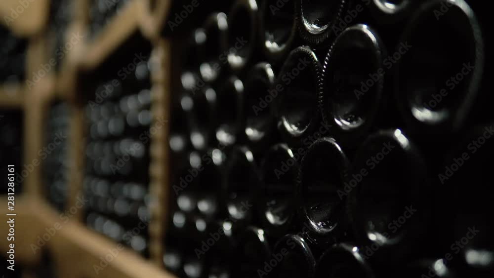 Wine bottles lying in stack at cellar. Glass bottles of red wine stored in wooden shelving in stone cellar. Interior underground wine cellar in winery