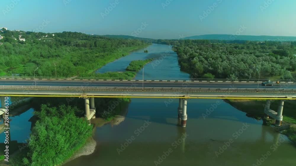 Aerial view of a car moving fast along bridge road over the tranquil river. 4K. Aerial view of a car moving fast along bridge road over the tranquil river. 4K.