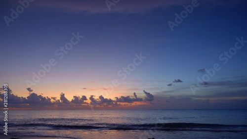 Dark blue sunset in ocean from sandy beach with dramatic sky and clouds