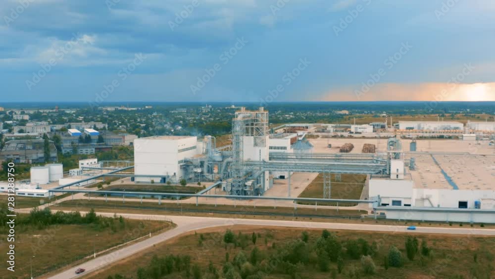Aerial circling view of a modern plant (factory) with pipeline, smoking chimney and workshop premises at sunset Aerial circling view of a modern plant (factory) with pipeline, smoking chimney and workshop premises at sunset