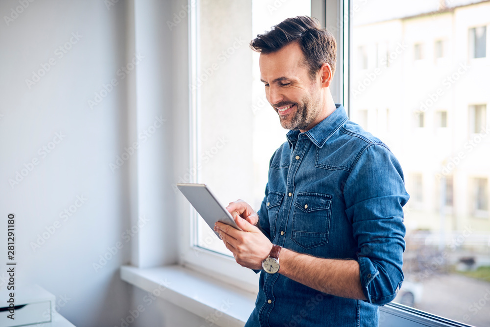 Smiling man using tablet at the window Smiling man using tablet at the window